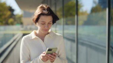 Ofis merkezinde yürüyen ve cep telefonu kullanan mutlu bir kadın.