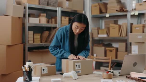 Trabalho preferido. Cintura para cima vista retrato da morena asiática adolescente mulher de pé no armazém e colocando adesivo na grande parcela. Conceito de pequenas empresas. — Vídeo de Stock