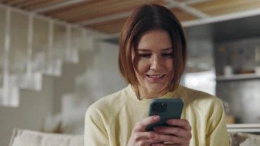 Kanepede oturup akıllı telefon kullanan hoş bir kadın.