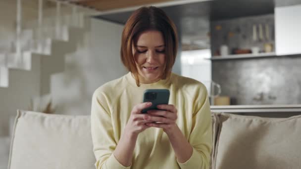 Mujer encantadora usando el móvil para chatear en línea en casa — Vídeo de stock