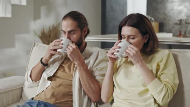 Пара сидящих вместе на диване и наслаждающихся горячими напитками — стоковое видео