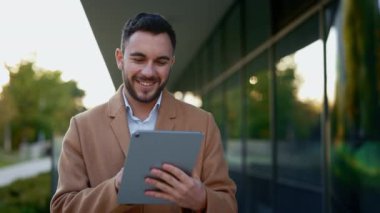 Kentsel alanda yürürken tablet kullanan gülümseyen işadamı