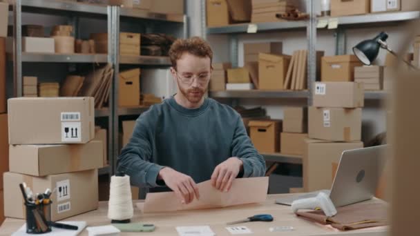 Opatrně, dělníku. Obraťte se na portrét moderního bělocha sedícího ve své kanceláři a balícího balík na řemeslném papíru. Muž balí noviny. Koncept malého podnikání. — Stock video