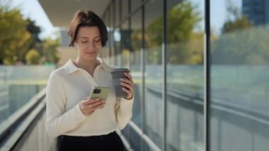 Ofis merkezinde cep telefonu kullanan ve kahve içen bir kadın.