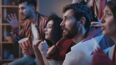 Evde Katar bayraklarıyla oturup televizyon izlerken tezahürat yapan mutlu futbol taraftarları. Genç insanlar içeride zafere bayram ediyorlar. Heyecan ve mutluluk kavramı.
