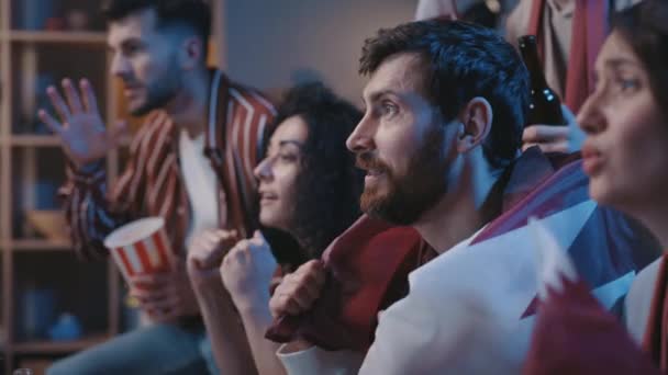 Boldog izgatott focirajongók otthon ülnek Katar zászlókkal és éljenznek, miközben TV meccset néznek. A fiatalok otthon örvendeznek a győzelemnek. Izgalom és boldogság koncepció. — Stock videók