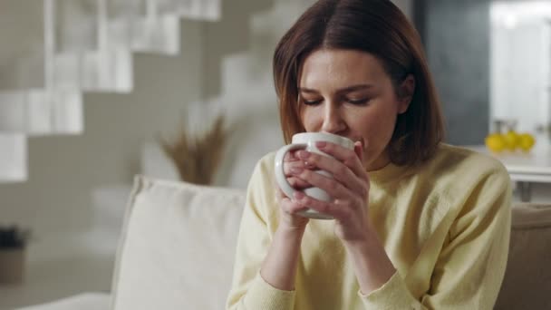 Przyjemna kobieta siedzi na kanapie i pije gorącą herbatę — Wideo stockowe