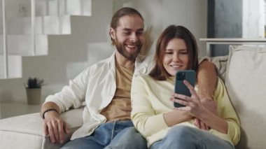 Pozitif aile elinde akıllı telefonuyla kanepede oturuyor.