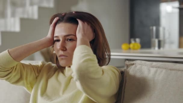 Расстроенная женщина сидит одна со своими мыслями на диване — стоковое видео