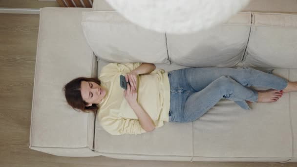 Ovanifrån av kvinna som använder smartphone när du ligger på soffan — Stockvideo