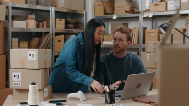 Mujer asiática poniendo en la pantalla del ordenador portátil con el dedo mientras discute algo con su colega caucásico mientras trabajan en la oficina del hogar. Concepto de pequeña empresa. — Vídeos de Stock