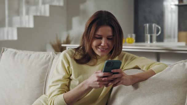 Sorrindo senhora sentada no sofá e mensagens de texto no smartphone — Vídeo de Stock