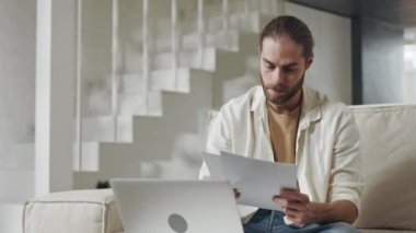 Belgeleri okuyan ve evde dizüstü bilgisayarda yazan odaklanmış bir adam.