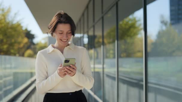 Mujer sorprendida recibiendo grandes noticias en el teléfono inteligente al aire libre — Vídeos de Stock
