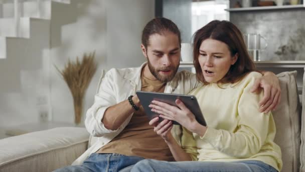 Веселая пара обнимается, получая хорошие новости на планшете — стоковое видео