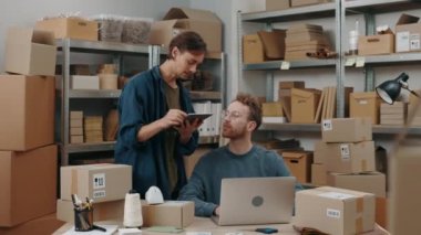 Esmer adam, erkek arkadaşıyla konuşuyor ve depodaki teslimat kutusunu hazırlarken tabletine bazı ayrıntılar yazıyor. Posta servisi ve küçük işletme kavramı.