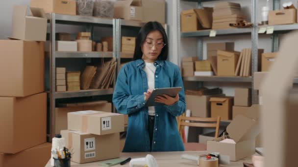 Dělnice v brýlích, která stála ve své kanceláři a psala do tabletu detaily s vážným obličejem. Poštovní služba a koncept malého podnikání. — Stock video