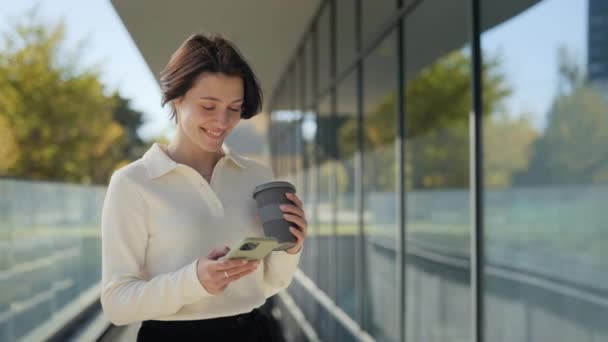 खुश महिला कॉफी पी रही है और मोबाइल आउटडोर का उपयोग कर — स्टॉक वीडियो
