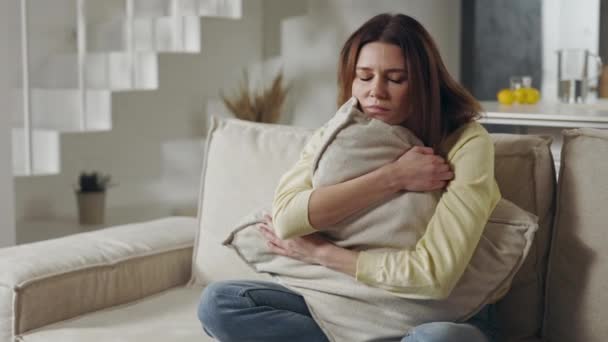 Mujer ansiosa en ropa casual abrazando almohada en el sofá mientras mira en la pantalla móvil. Caucásico persona femenina con ansiedad alojarse en apartamento moderno. — Vídeo de stock