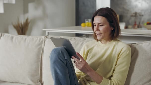 Attraktiv kvinna sitter på soffan och använder digital tablet — Stockvideo