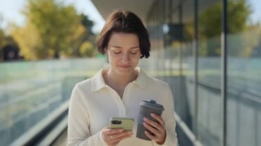 Kahve içen ve iş merkezinin yakınında cep telefonu kullanan bir kadın.