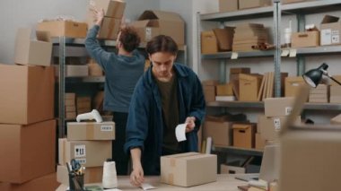 Beyaz erkek meslektaşların paket paketlediği ve merkez büroda çalışırken etiketlerini yapıştırdığı belden portre görüntüsü. Posta servisi ve küçük işletme kavramı.