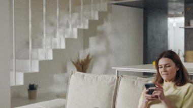 Pozitif kadın koltukta oturuyor ve akıllı telefon kullanıyor.