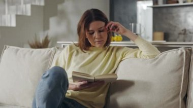 Ev hanımı rahat koltukta otururken kitap okuyor.