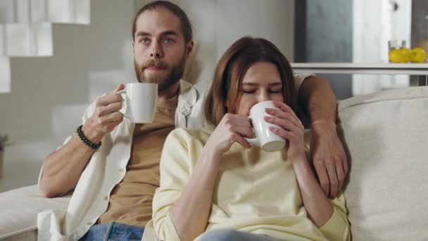 Красивая пара пьет чай, отдыхая на удобном диване — стоковое видео