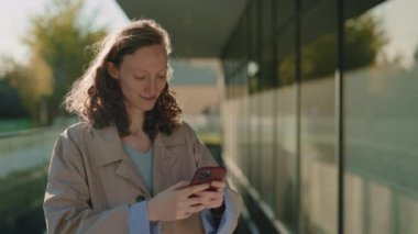 Akıllı telefondan mesaj atarken dışarıda gülümseyen çekici bir kadın.