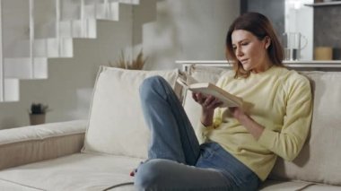 Çekici kadın elinde kitapla kanepede dinleniyor.