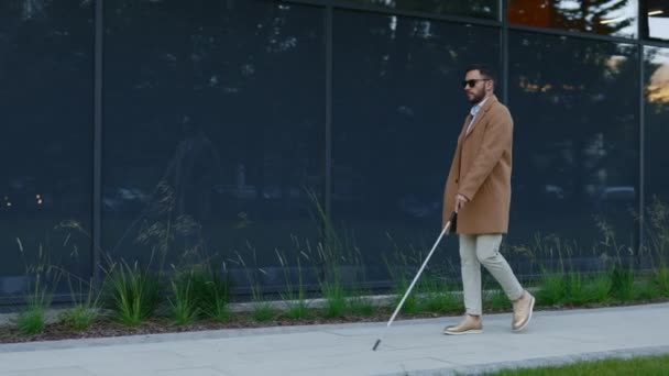 Homme aveugle caucasien en tenue élégante en utilisant la canne pour la promenade de sécurité dans la rue de la ville. beau mâle personne vérifier direction avec bâton à l'extérieur. — Video