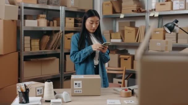 Talje op portræt visning af den kvindelige lager arbejdstager ved hjælp af smartphone og skydning parcel, mens du forbereder sende den til kunden. Små og mellemstore virksomheder. – Stock-video