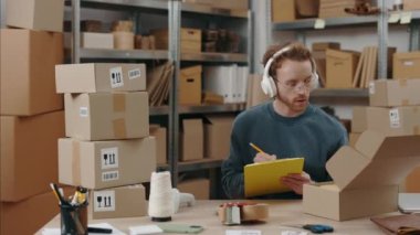 Dosyaya bir şey yazan ve müşteriye paket göndermeye hazırlanan Kafkasyalı girişimci sakin. Depoda çalışan ve müzik dinleyen adam. Küçük işletme kavramı.