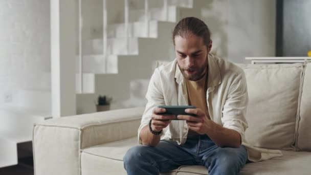 Счастливый человек использует смартфон для игры дома — стоковое видео