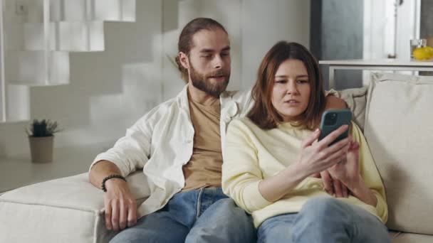 Dua orang jatuh cinta menggunakan smartphone saat beristirahat di sofa — Stok Video