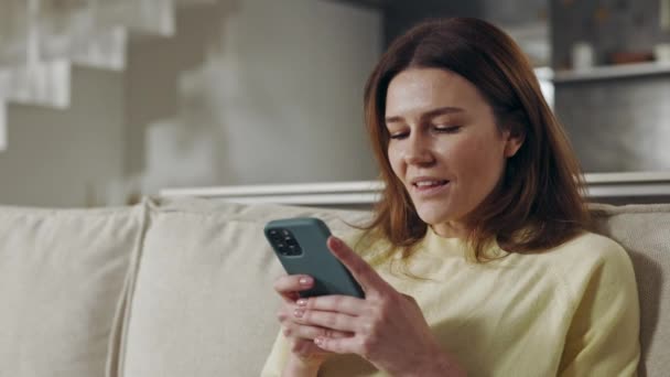 漂亮的女人坐在沙发上用智能手机 — 图库视频影像