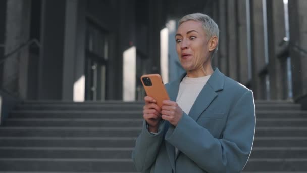 Joyful caucasian business woman with smartphone in hands emotionally gesturing while celebrating her success at work. Victory, lottery, technology and people concept. — Stock Video