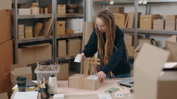 倉庫で一人で働いている間のブルネットの郵便配達の女性のスキャン小包のウエストアップ肖像画ビュー。背景に箱がある棚。郵便サービスと小規模なビジネスコンセプト. — ストック動画