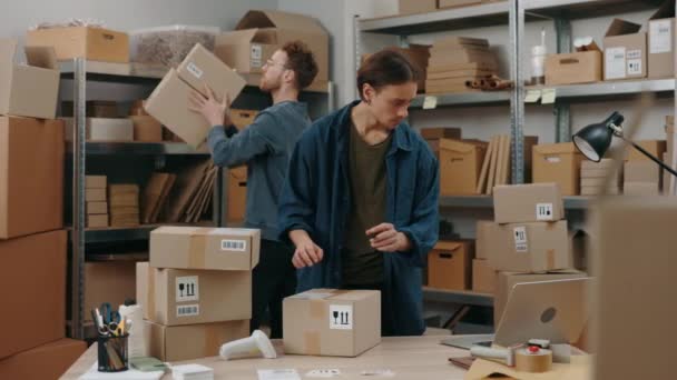 Caucasian postman and his male colleague putting stickers at the cupboard box while preparing delivery parcel box. Post service and small business concept. — Stockvideo