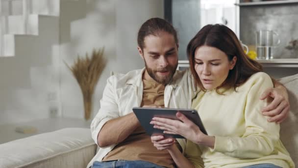 Couple sitting on couch and reading good news on tablet — ストック動画