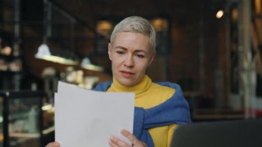 Kafe masasında elinde belgeler ve laptopla oturan bir kadın.
