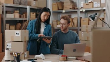 Girişimciler siparişleri kontrol ediyor ve depodaki teslimat kutusunu hazırlarken tablete bazı ayrıntılar yazıyorlar. Posta servisi ve küçük işletme kavramı.