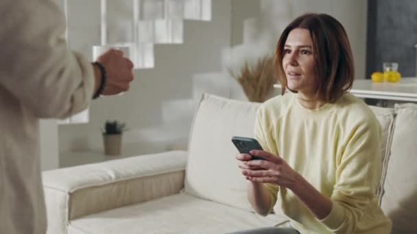 Man bringing tea to wife that using mobile on couch — Vídeos de Stock