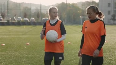 Antrenmandan sonra yürüyen ve konuşan iki bayan futbolcu.