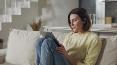 Kanepede oturan ve dijital tablet kullanan kadın.