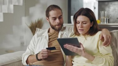 Tableti ve kredi kartı olan çift evde alışveriş yapıyor.