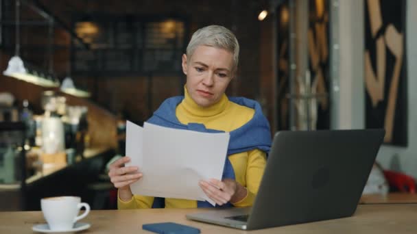 Vrouw die documenten onderzoekt en laptop gebruikt in café — Stockvideo