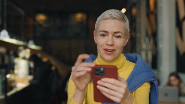 Έκπληκτη γυναίκα διαβάζει καλά νέα στο κινητό στο καφέ — Αρχείο Βίντεο