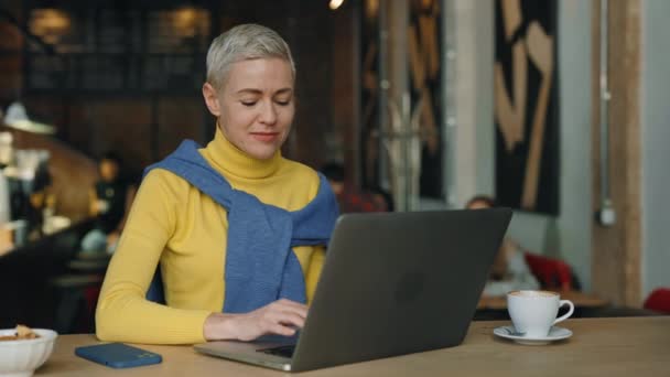 Donna positiva seduta al caffè e utilizzando il computer portatile per il lavoro — Video Stock
